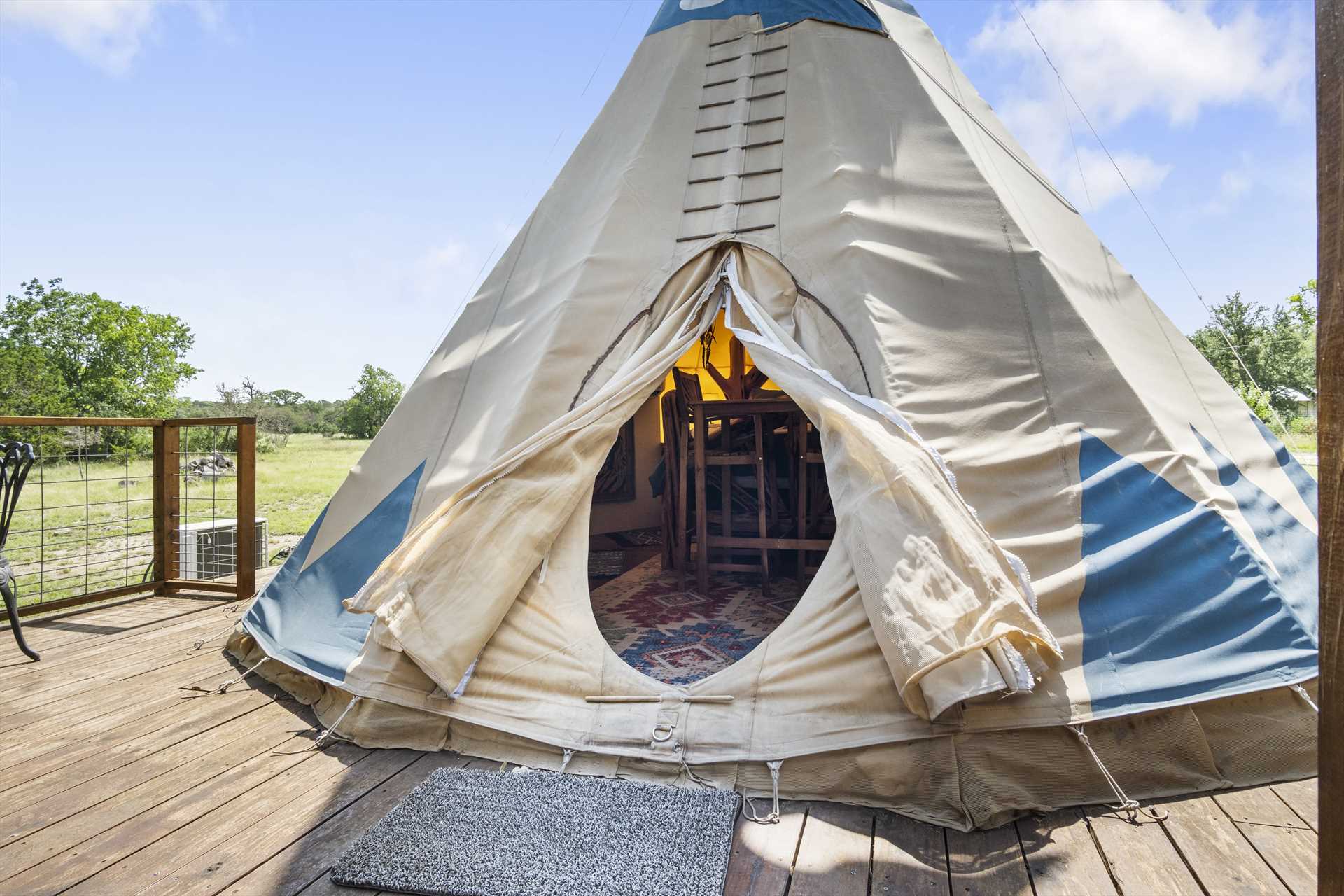 A stylish teepee entrance on a wooden deck, revealing a glimpse of the cozy interior. Surrounded by lush greenery, it invites outdoor adventure.