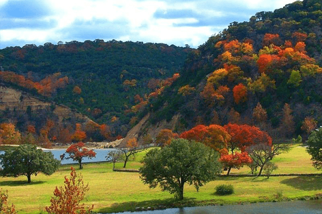 Vibrant autumn foliage covers hills and trees beside a tranquil lake, showcasing nature’s beauty in a serene landscape.